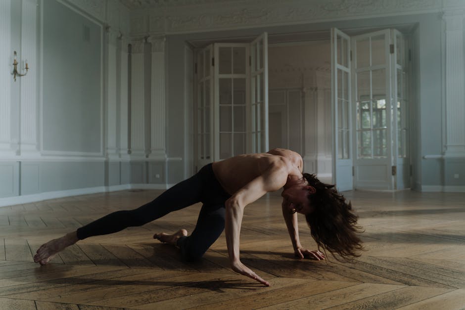 Shirtless dancer performing in a spacious room with elegant decor and wooden floors.