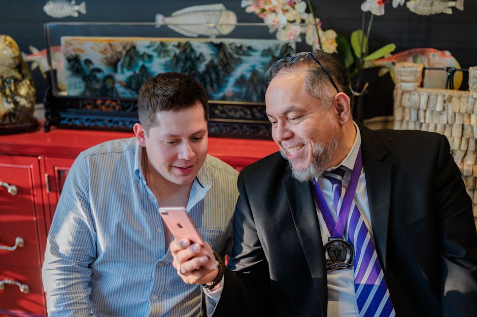 Two men smiling as they look at a smartphone indoors, showcasing technology and connection.