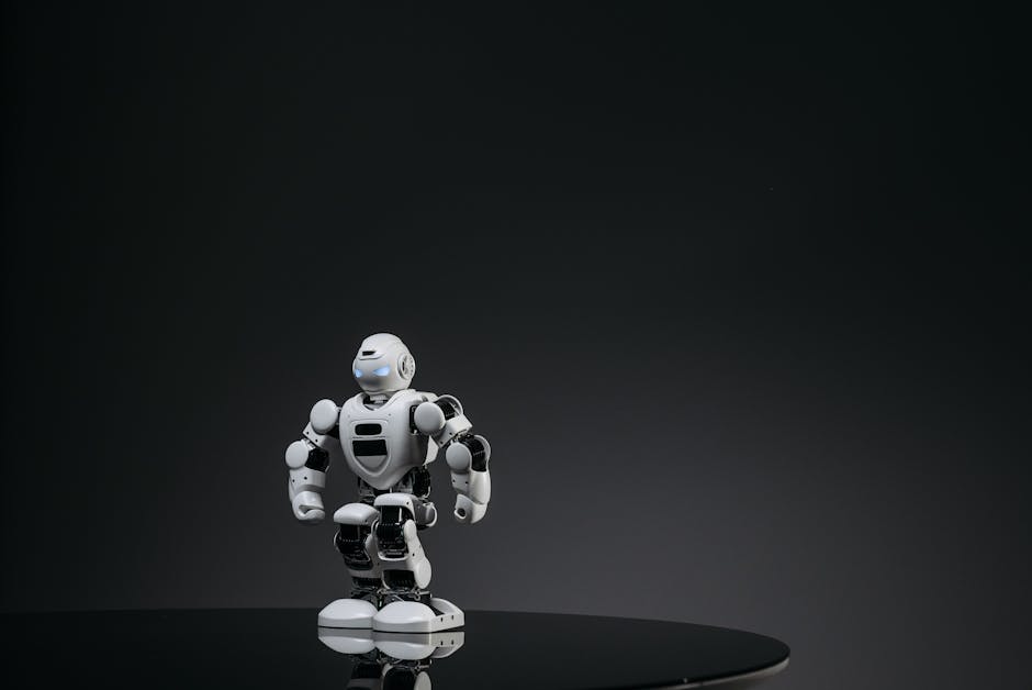 A small white robot stands on a reflective surface in a dark studio setting, showcasing modern technology.