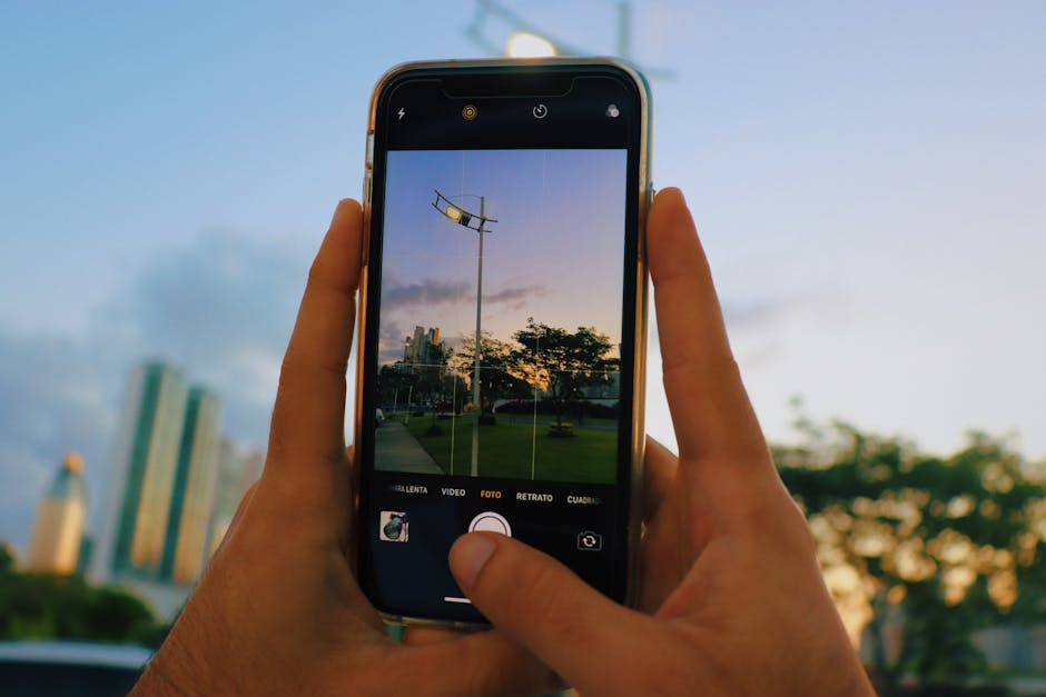 A close-up shot of a smartphone taking a photo of a city skyline during sunset.
