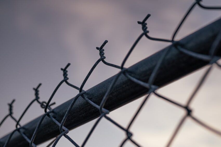 Artistic close-up of a metal chain-link fence against a twilight sky, conveying solitude.